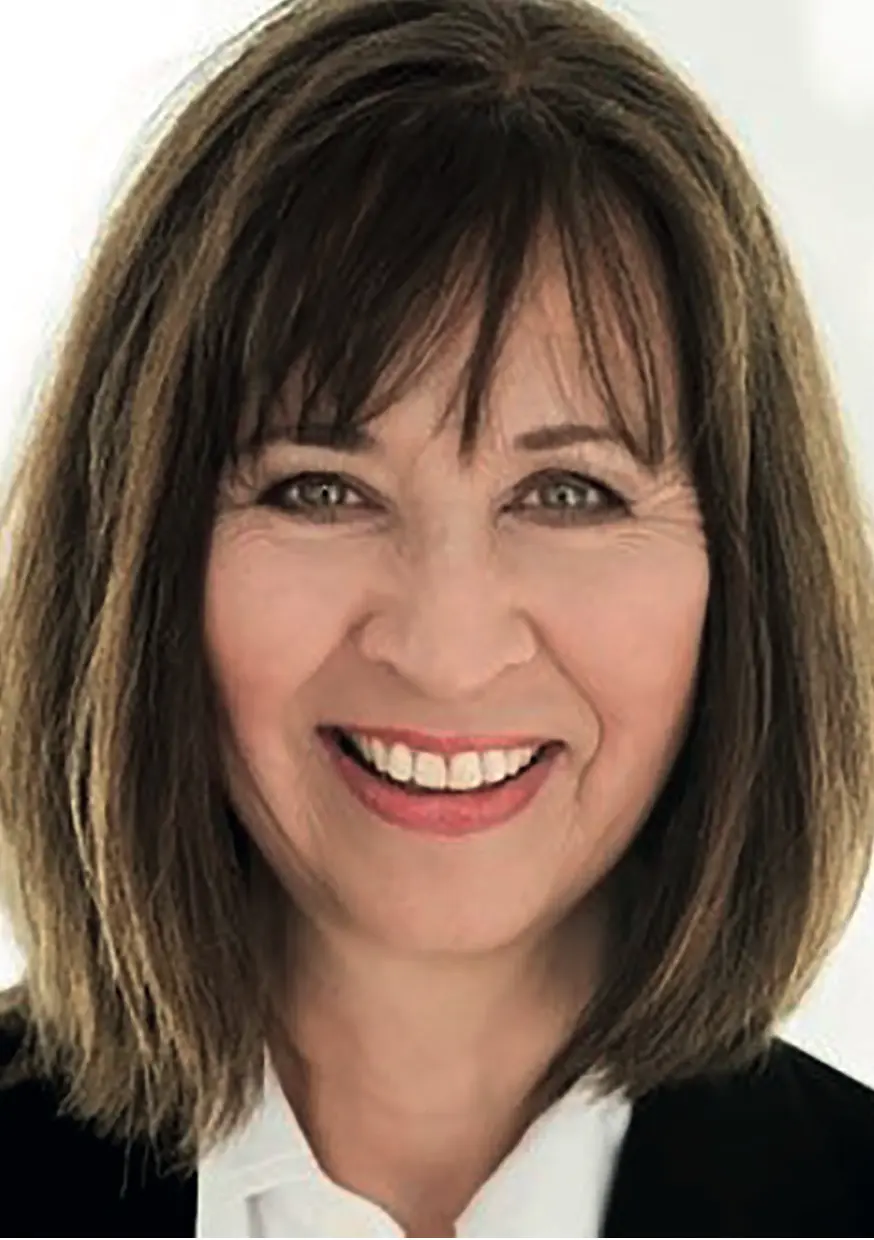 Person mit schulterlangem braunem Haar lächelt in die Kamera.