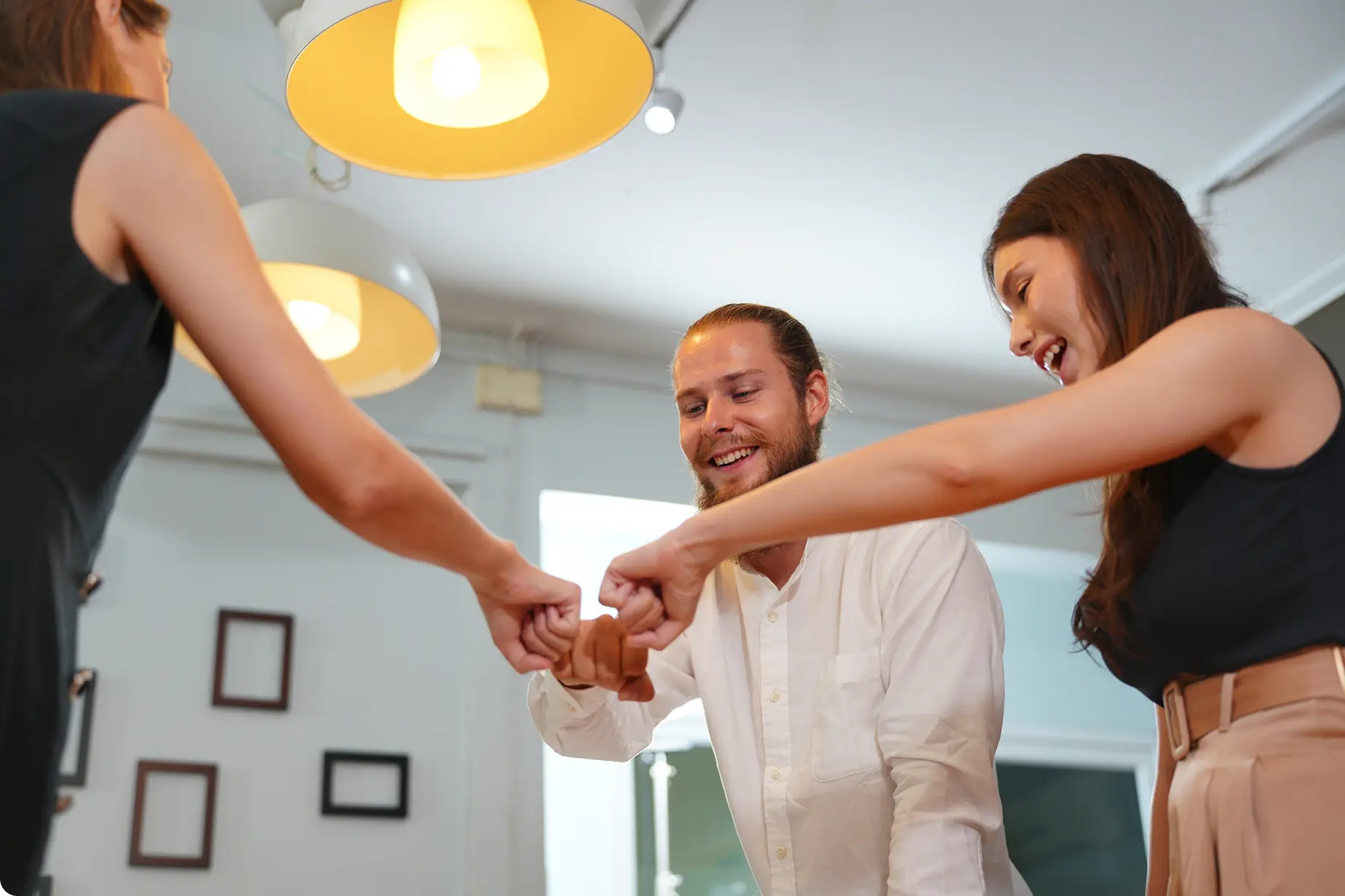 Drei Personen lächeln und machen einen Fistbump in einem hellen Raum.