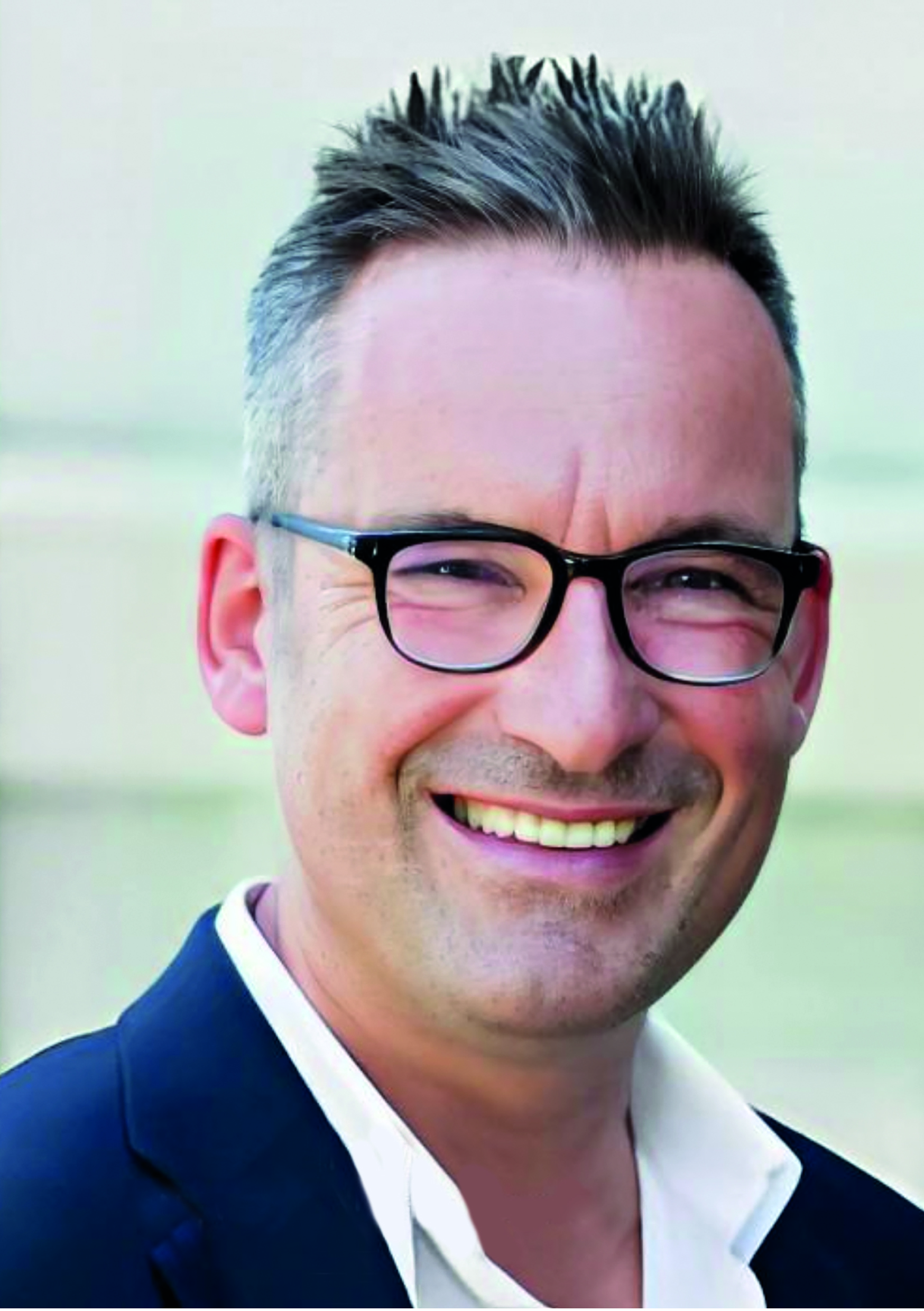 Mann mit Brille und kurzem Haar lächelt in die Kamera.