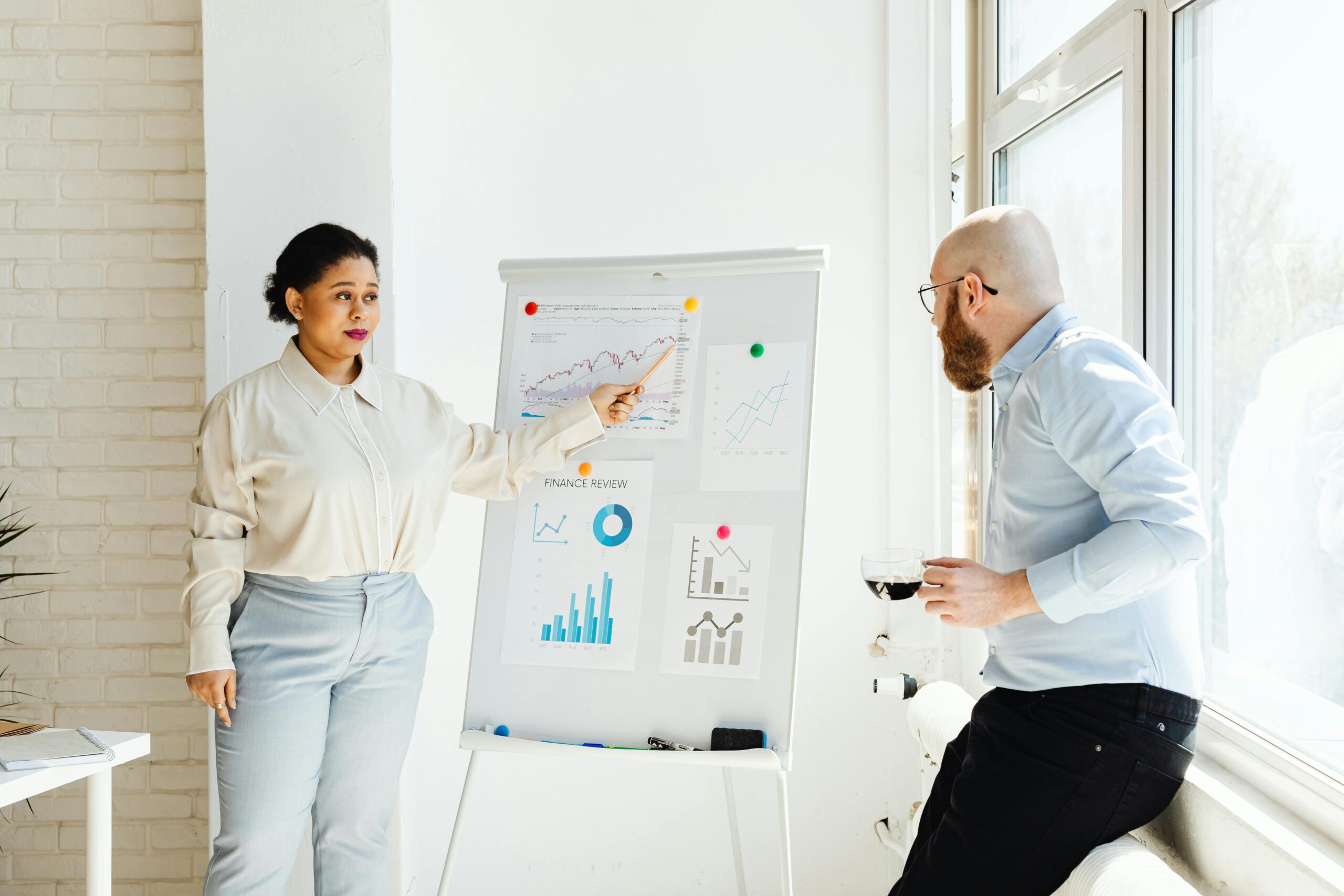 Zwei Personen diskutieren vor einem Flipchart mit Diagrammen in einem hellen Raum.
