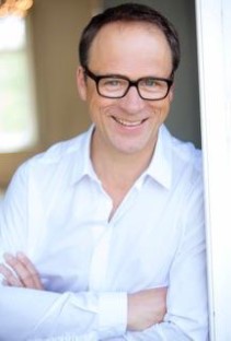 Mann mit Brille und weißem Hemd lächelt in die Kamera.