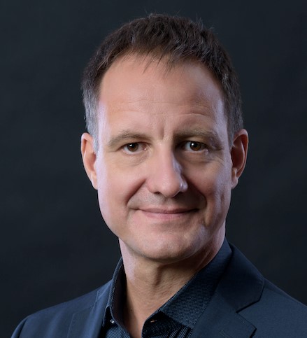 Eine Person im Anzug vor dunklem Hintergrund.