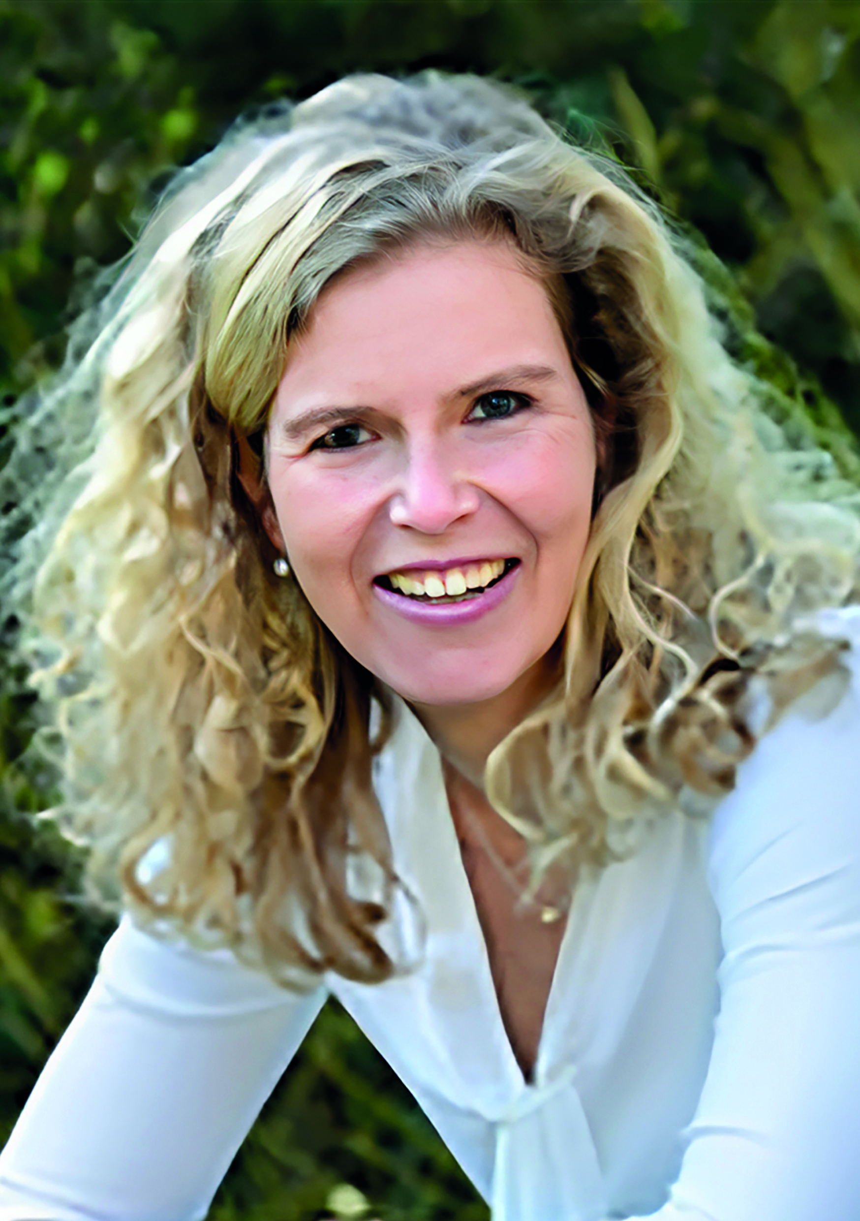 Eine lächelnde Person mit lockigem Haar in weißer Bluse vor grünem Hintergrund.