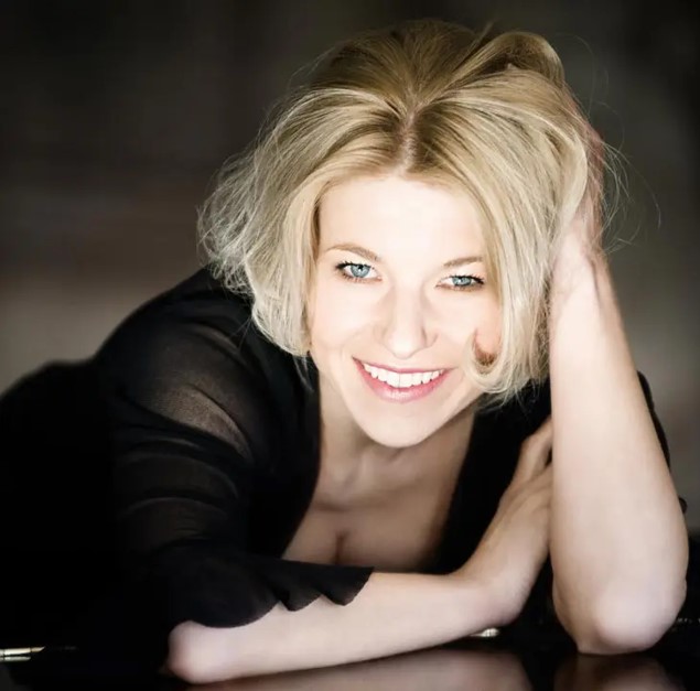 Eine lächelnde Person mit blonden Haaren liegt auf einer dunklen Oberfläche.