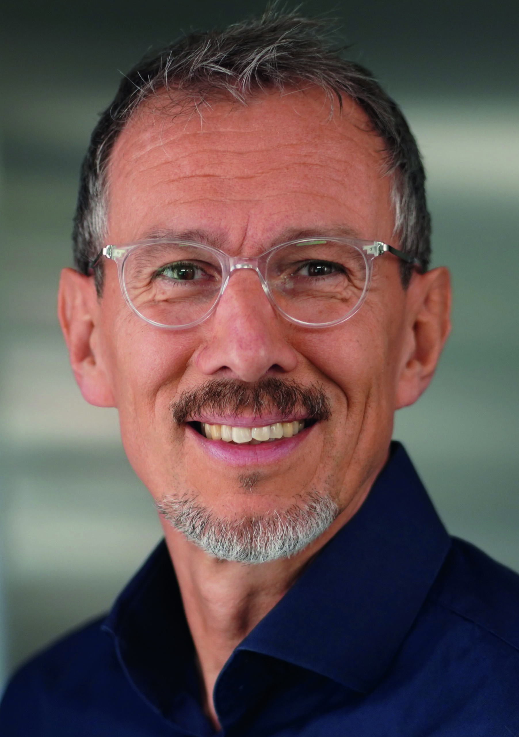 Mittelalter Mann mit Brille und Bart lächelt in die Kamera vor unscharfem Hintergrund.