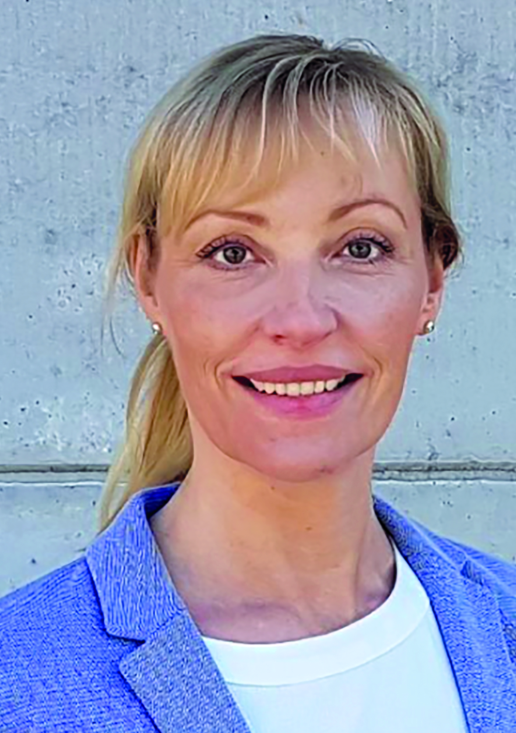 Eine lächelnde Frau vor einer grauen Betonwand.