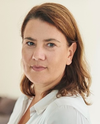 Eine Frau mit braunem Haar und weißer Bluse blickt in die Kamera.